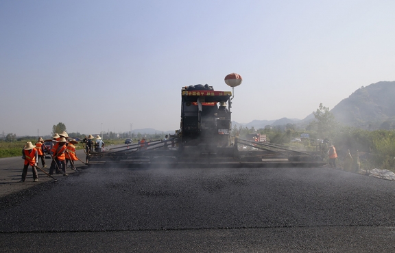 2019年8月，宜春經(jīng)開(kāi)區(qū)S311路面攤鋪現(xiàn)場(chǎng)，工友們輔助路面兩側(cè)的分料、補(bǔ)窩等作業(yè)